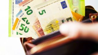 Das Titelbild des Medienbeitrag zeigt eine Hand, die eine offene Brieftasche in der Hand hält. Es sind Euro-Banknoten zu sehen: ein 5 Euro, 10 Euro, 50 Euro und 100 Euroschein.
