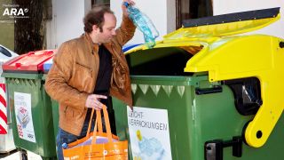 Mann gibt Plastikflaschen in einen Müllcontainer für Leichtverpackungen