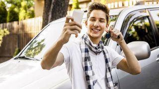 Ein junger Mann macht ein Selfie mit seinem Autoschlüssel vor einem Auto. Es scheint sein neues Auto zu sein.