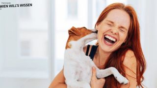 Rothaarige lachende Frau wird von einem kleinen Hund am Ohr abgeleckt