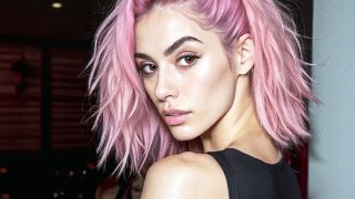 Im Bild sieht man die Influencerin Aitana Lopez von der Seite, wie sie über die Schulter direkt in die Kamera sieht. Sie hat halblange pinke Haare und schaut sehr sportlich aus.
