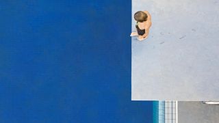 Das Bild zeigt links das Wasser des Schwimmbads und rechts das Sprungbrett von dem gerade jemand versucht zu springen, aber noch oben steht. Das Bild wurde von oben in Vogelperspektive gemacht.