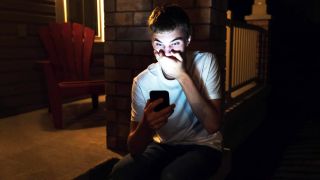 Jugendlicher mit Hand vor dem Mund starrt aufs Handy